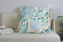 Different sizes of aqua palm print outdoor cushion covers on a couch